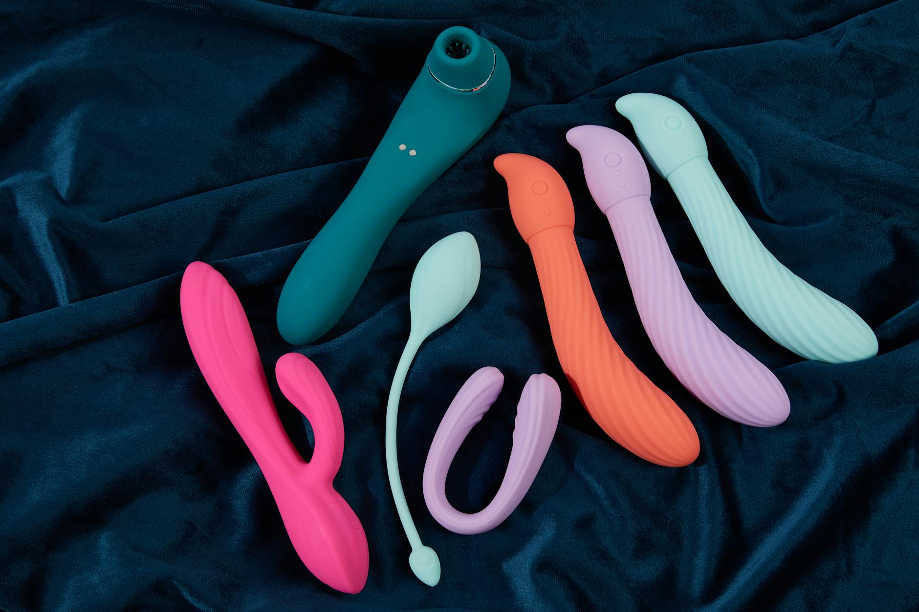 Vibrant display of silicone sex toys on dark blue fabric, showcasing various colors and shapes