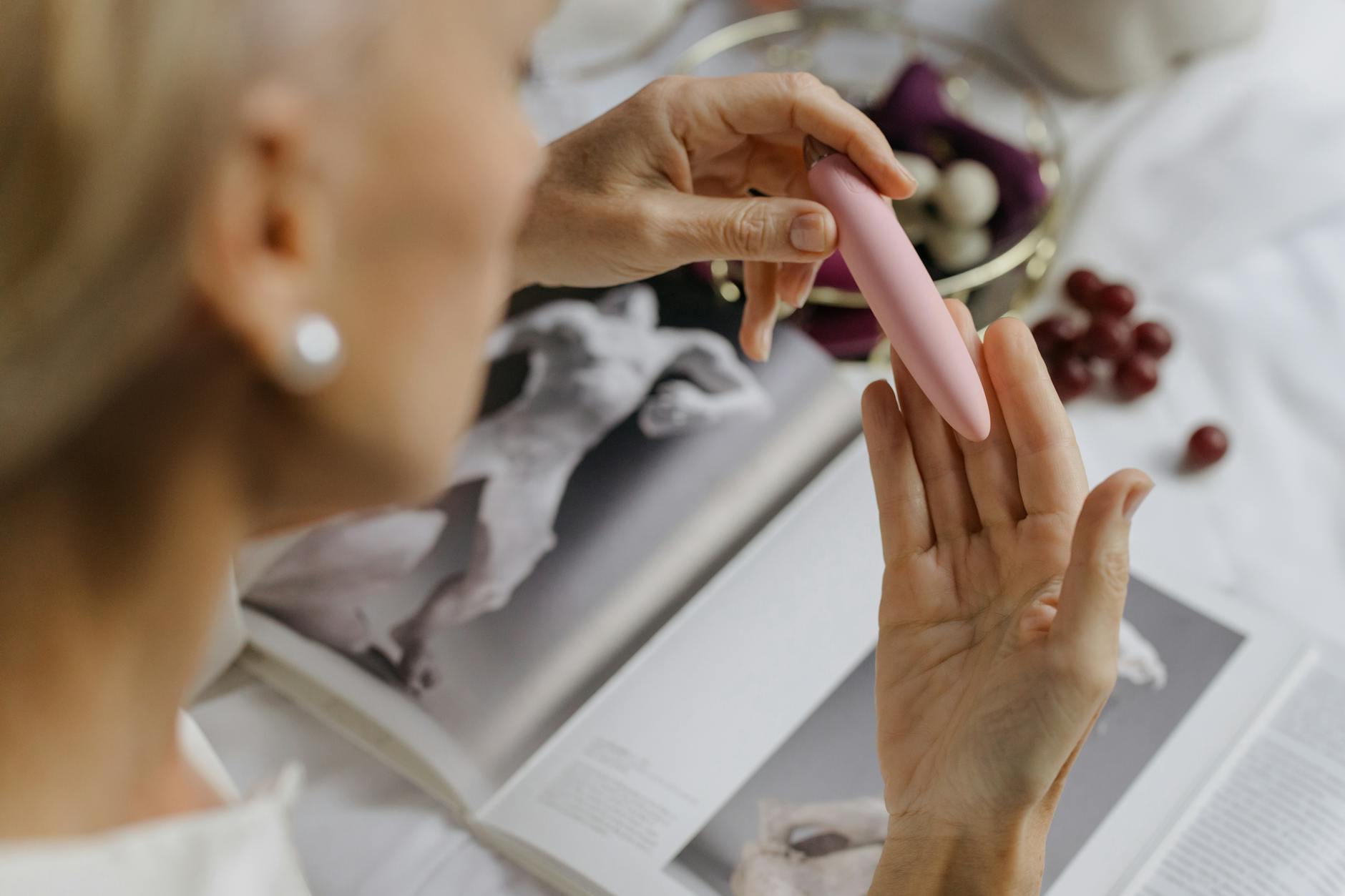 Close-up of a woman holding a pink vibrator with personal items in background, representing intimate postpartum healing