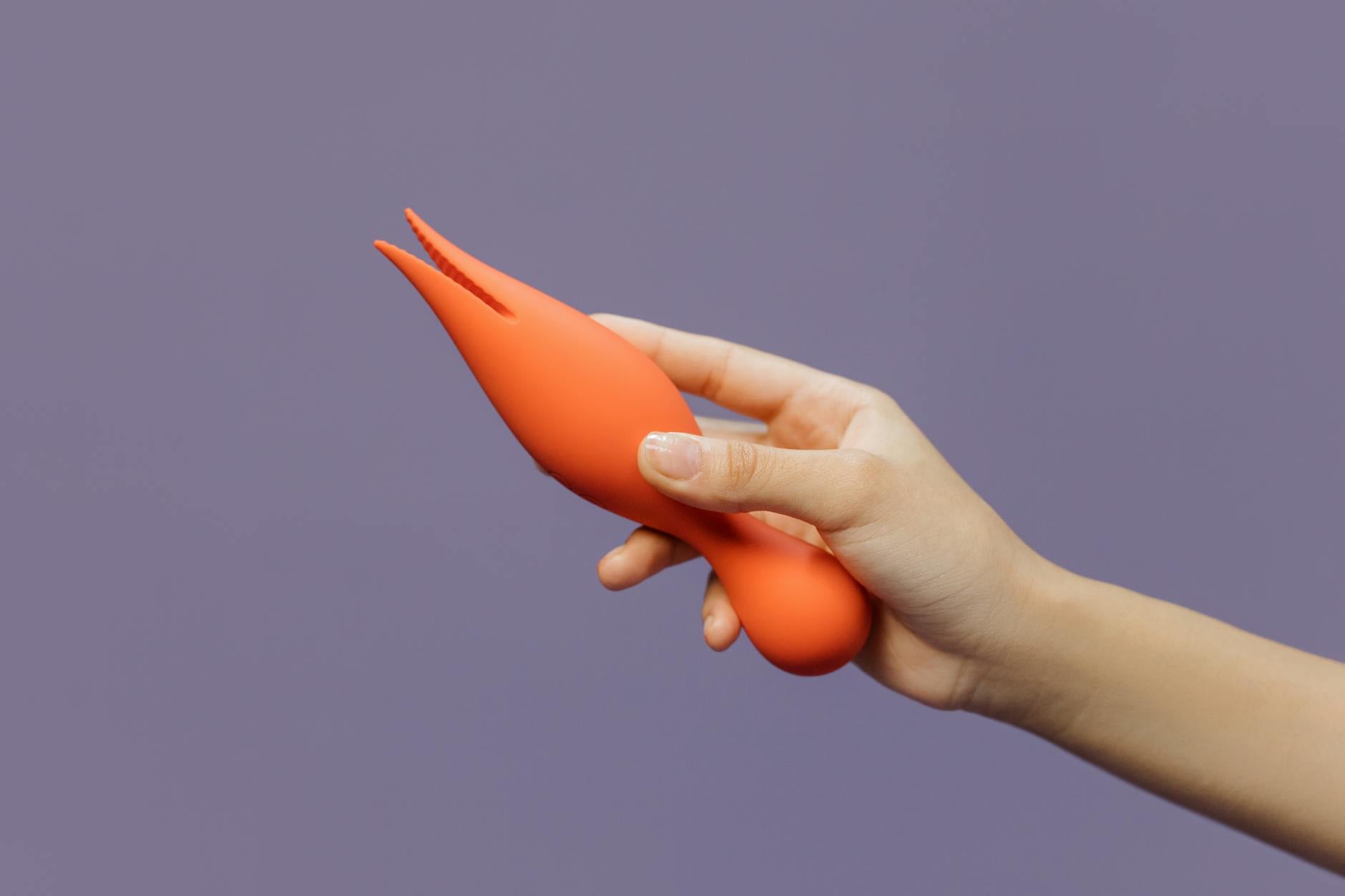 A hand holding a vibrator against a minimalist purple backdrop, representing solo pleasure and self-care